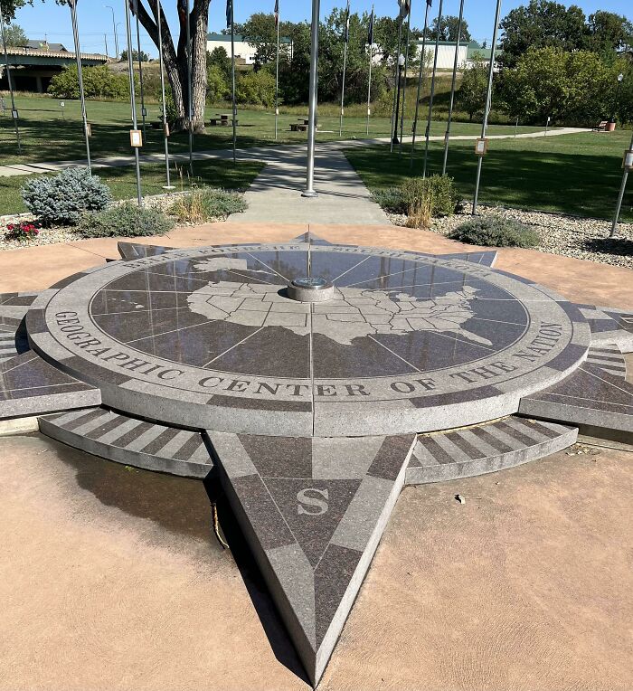 "Iconic geographic center monument in the United States, surrounded by flags in a park setting."