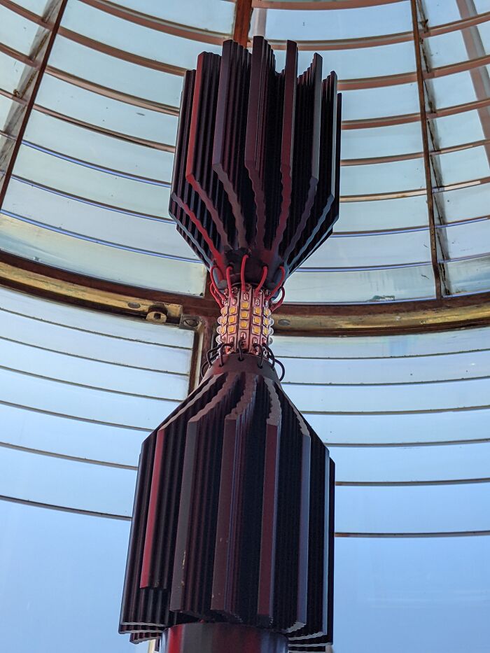 Intricate lighthouse light mechanism under a domed glass ceiling, showcasing engineering at an iconic place.