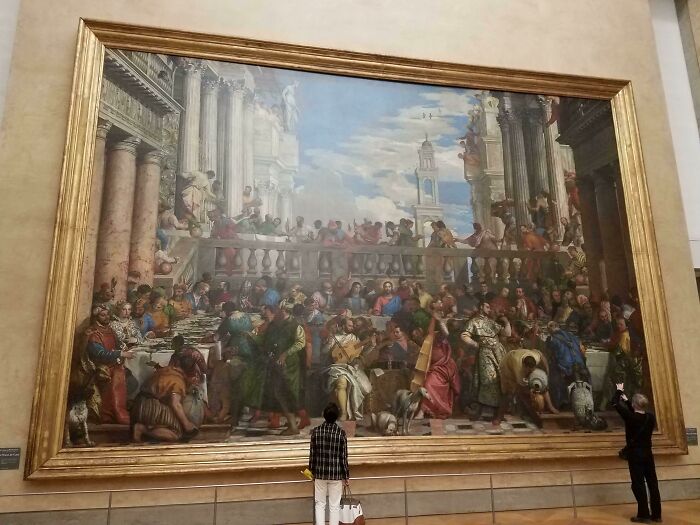People admiring a large, iconic painting displayed in a museum gallery, depicting a historical scene.