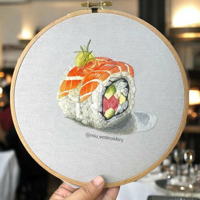 Hand holding embroidery hoop showcasing detailed and beautiful sushi embroidery skill on neutral fabric.