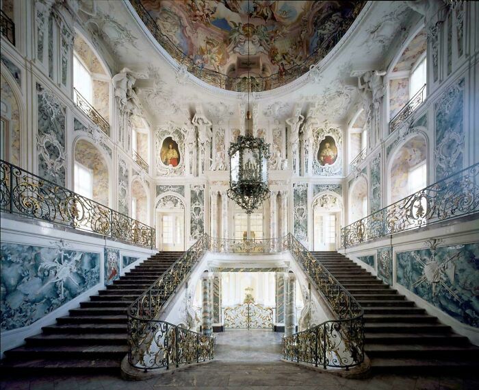 Ornate grand staircase in a baroque interior showcasing impressive architectural feats and intricate decorative details.