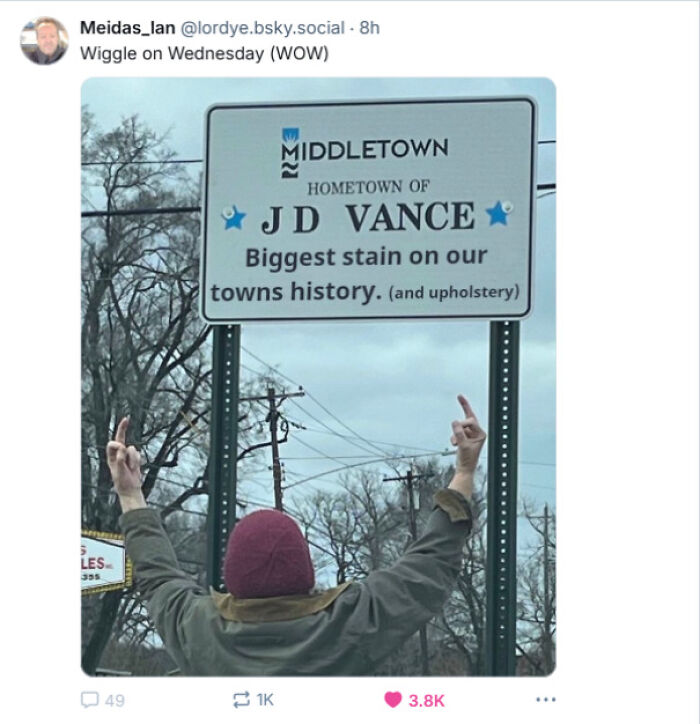 Person showing middle fingers at a modified town sign in Middletown, reflecting courage to tweet bold statements.