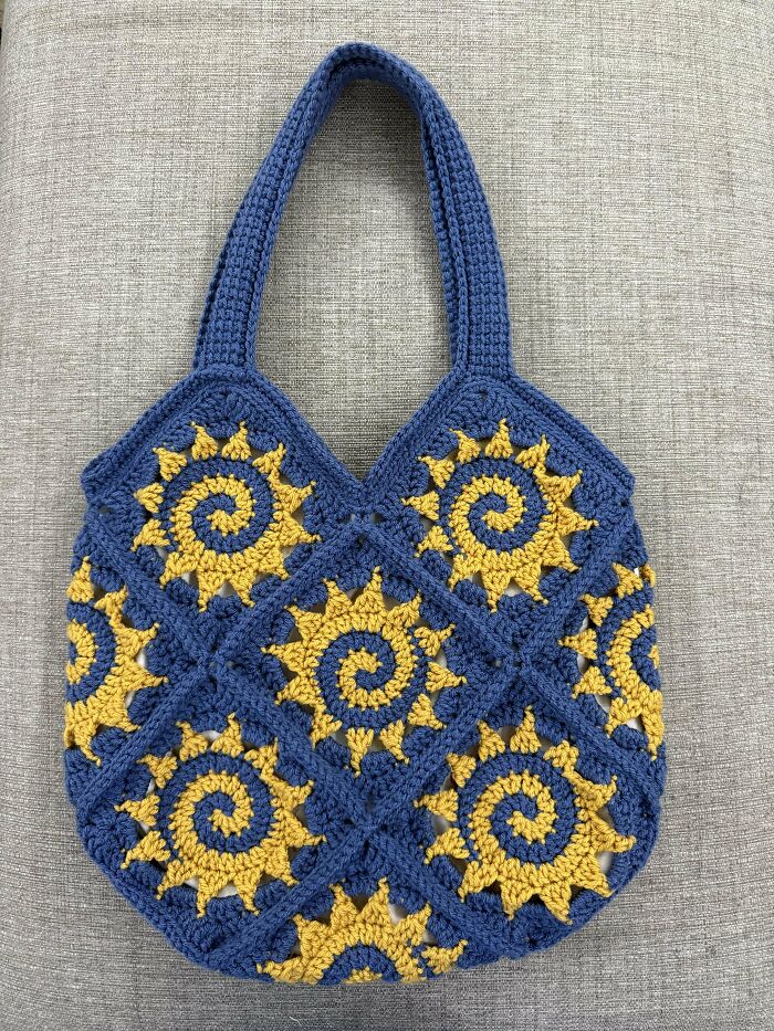Blue and yellow crochet bag with sun spiral pattern, showcasing incredible craftsmanship by crochet enthusiasts.