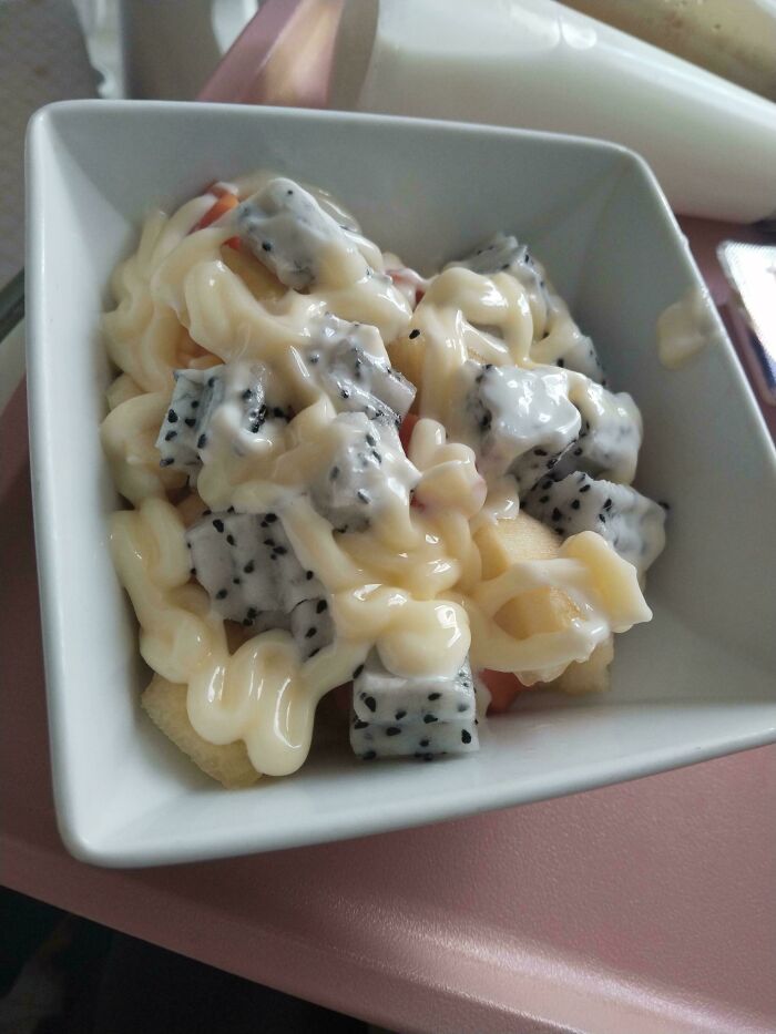 Bowl of diced dragon fruit and other fruits covered with a generous drizzle of creamy mayonnaise, a quirky dish example.