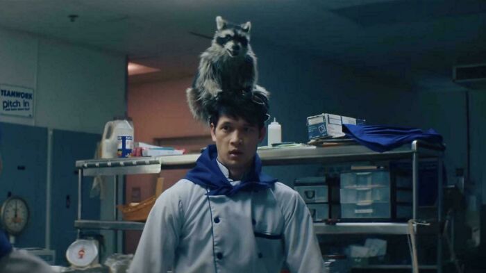 Man in chef uniform with raccoon on his head in a dimly lit kitchen, illustrating questionable movie details for cinephiles to mock.