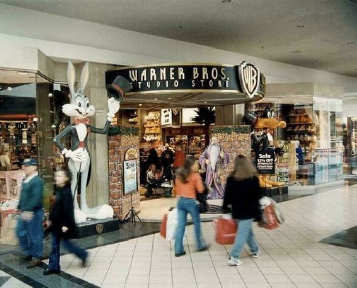 Shoppers walk past a Warner Bros store with large Bugs Bunny and Daffy Duck statues, evoking nostalgic 90s vibes.