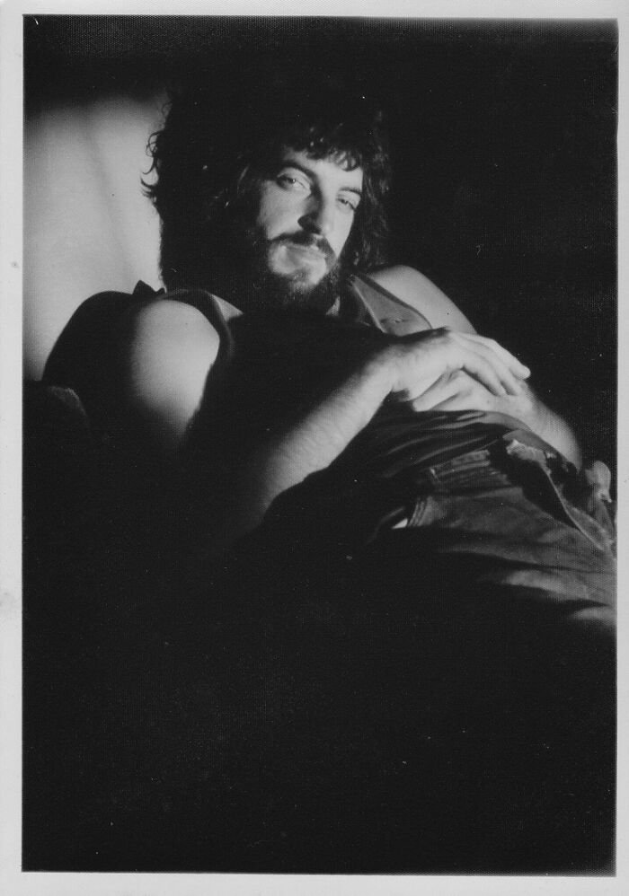 Black and white candid portrait of a relaxed man with beard and curly hair, capturing a rare glimpse into the past.