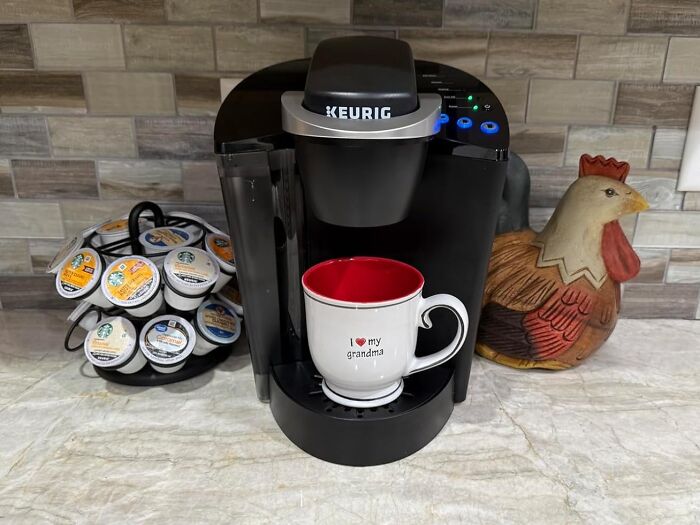 Keurig coffee maker with a mug that reads "I love my grandma," and a carousel of coffee pods in a kitchen setting.
