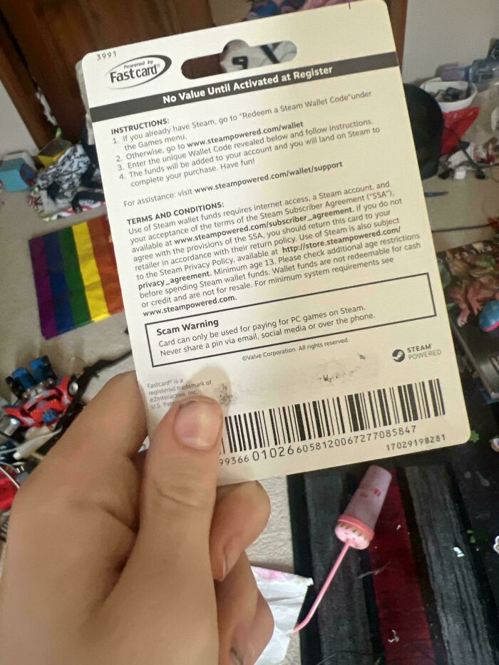 Person holding a Steam wallet card with terms, conditions, and scam warning visible.