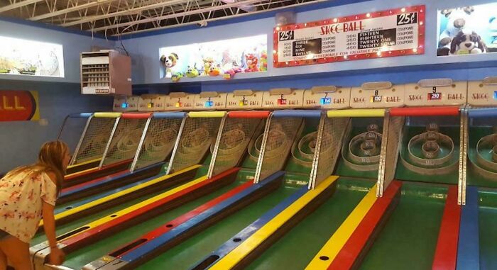 Woman playing vintage skee ball in a nostalgic arcade with colorful lanes and classic game signs visible on the wall.