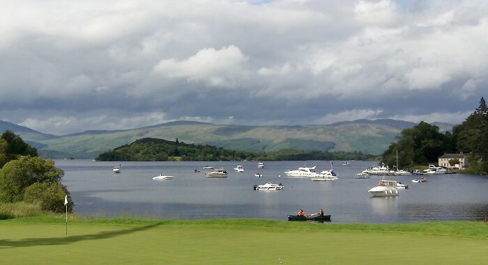 Golfers relish a stunning lakeside golf course with boats and hills in the background.