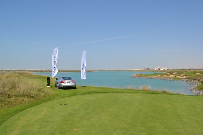 Scenic golf course with a luxury car near a serene water hazard under a clear blue sky.