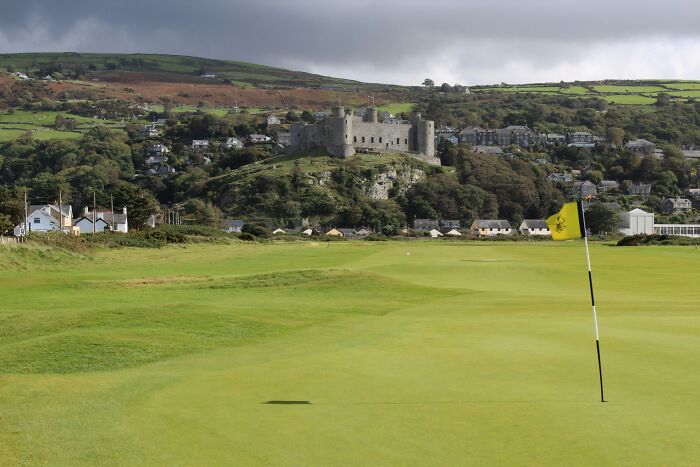 Golf course with flag, lush landscape, and historic castle in the background, highlighting breathtaking golfing destinations.