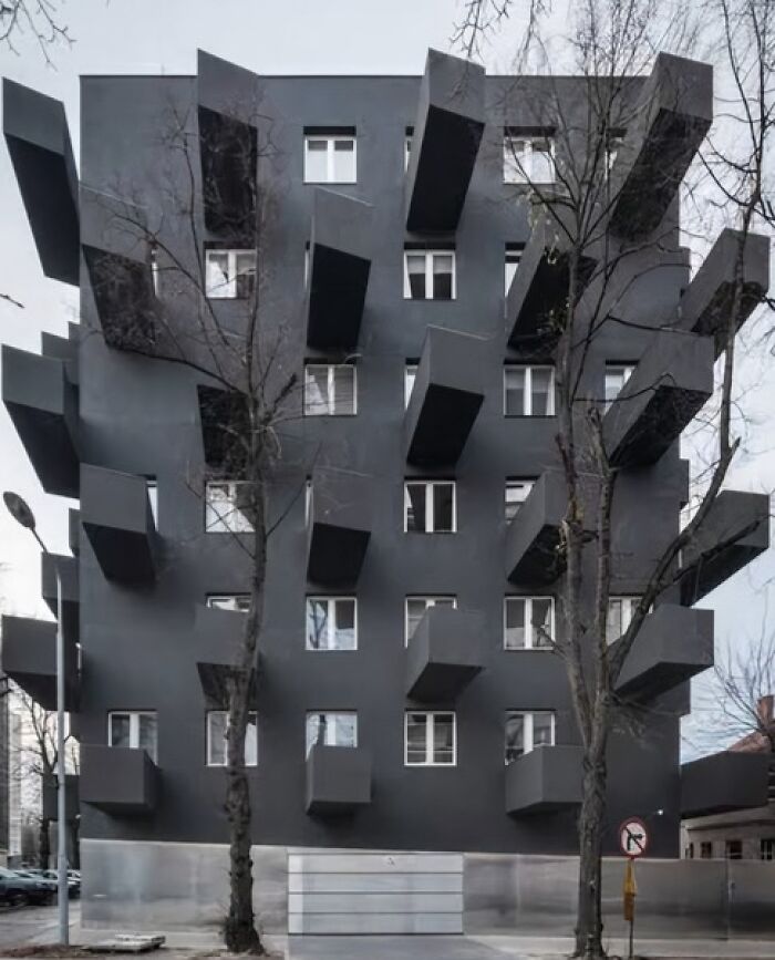 Edificio con diseño arquitectónico fallido y balcones extraños, rodeado de árboles en invierno.