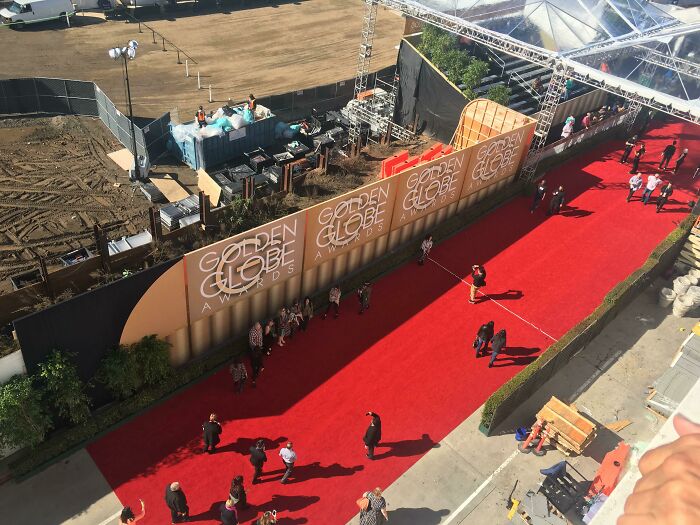 Red carpet at iconic Golden Globe Awards, viewed from above, with people walking towards event setup area.