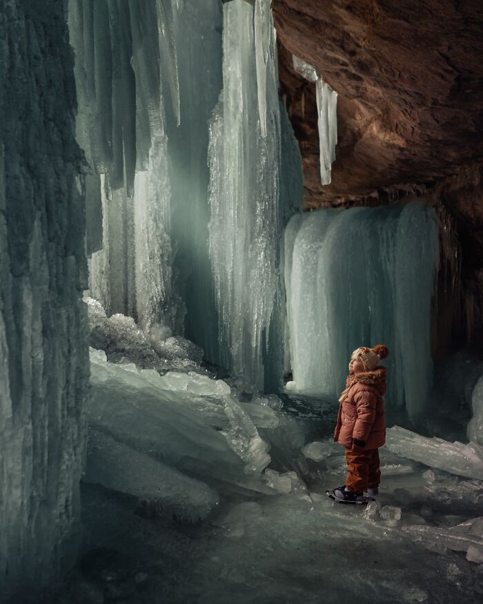 Child explores icy cave wonderland, captured through a mother's lens, embodying the magic of childhood.
