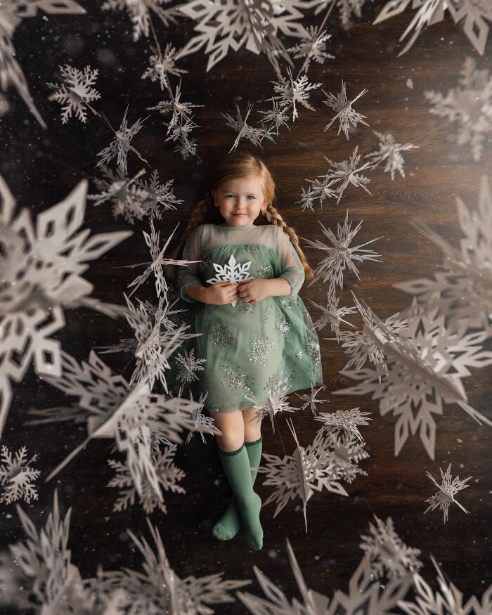 A child in a green dress surrounded by paper snowflakes, capturing the magic of childhood through a lens.