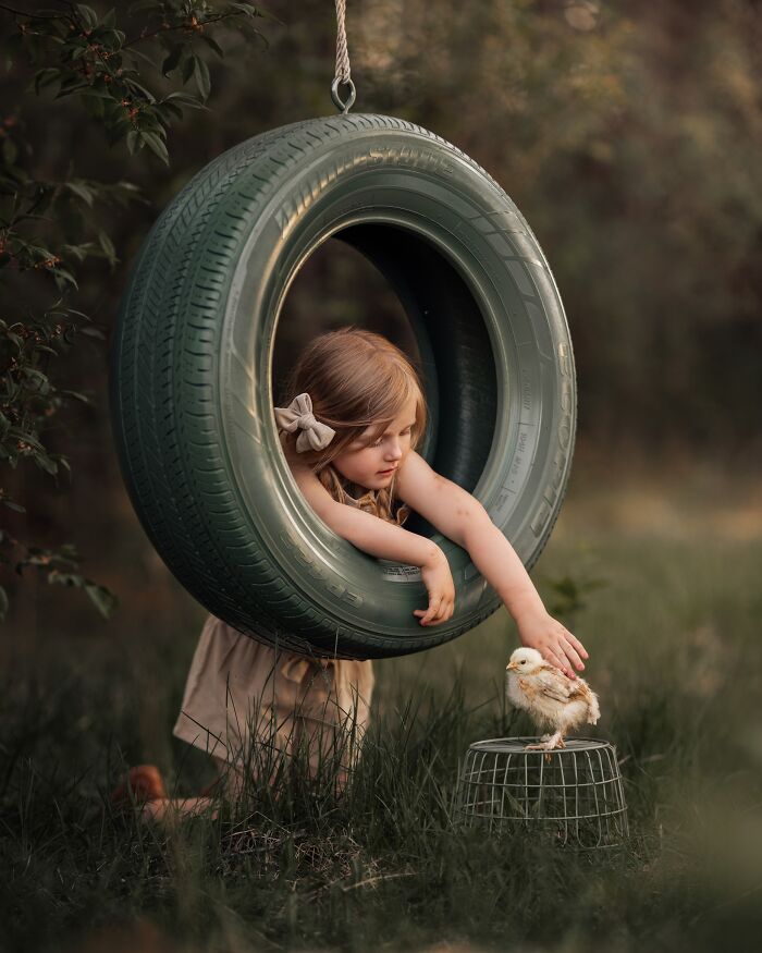 Childhood magic captured by mother: girl in tire swing reaches for chick in grass.