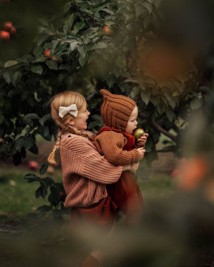 Two children in cozy outfits enjoying an apple orchard, capturing the magic of childhood through a mother's lens.