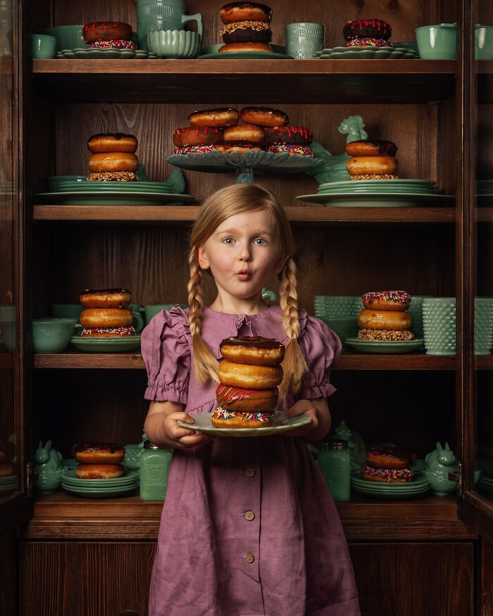 Young girl in pigtails holding a plate of donuts, surrounded by vintage cups and plates, capturing childhood magic.