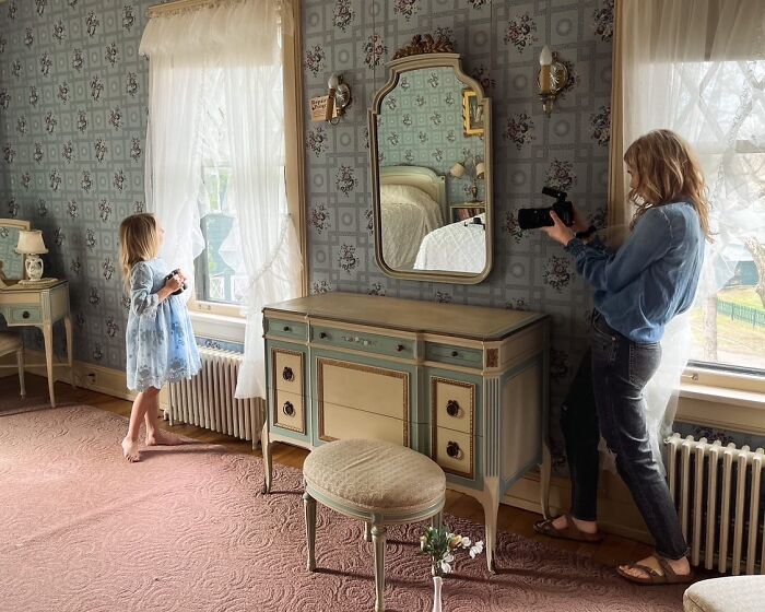 Mother captures childhood magic as daughter gazes out window in vintage room.