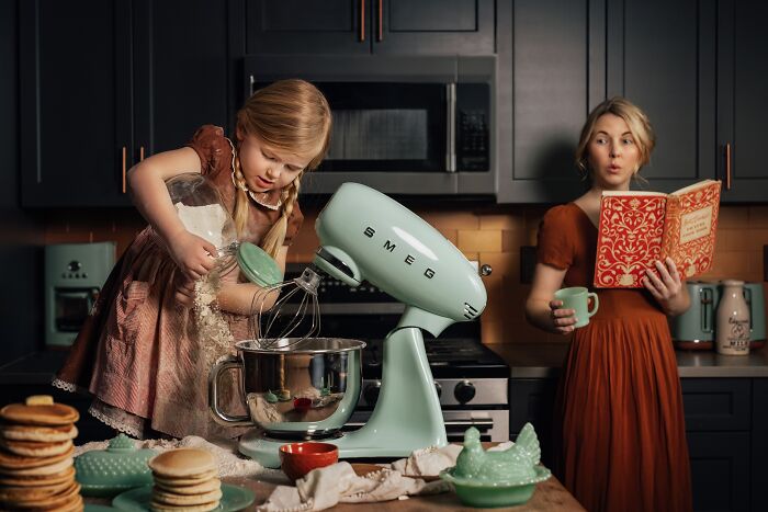 Childhood magic captured as a girl bakes using a mixer, with her mother holding a cookbook in the kitchen.
