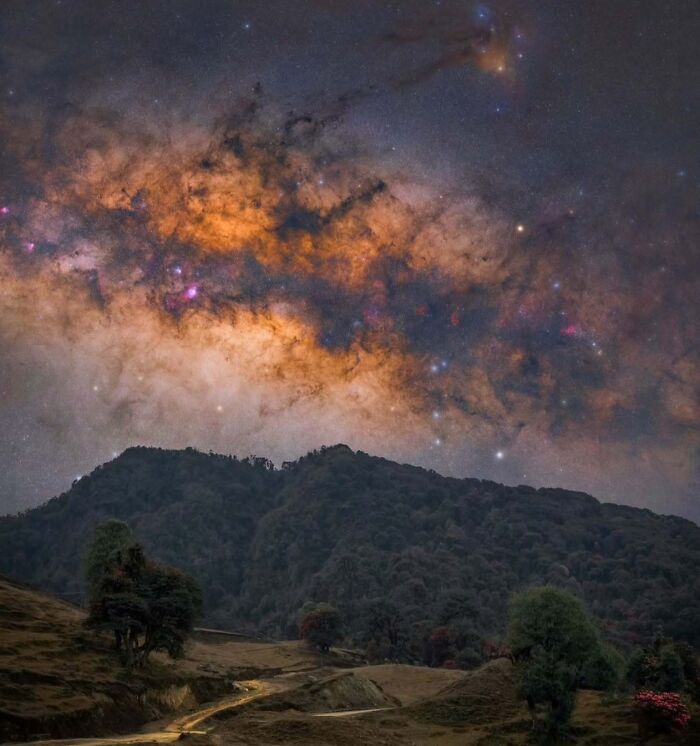 Astrophotography of a vibrant night sky with a luminous Milky Way over silhouetted hills and a winding pathway below.