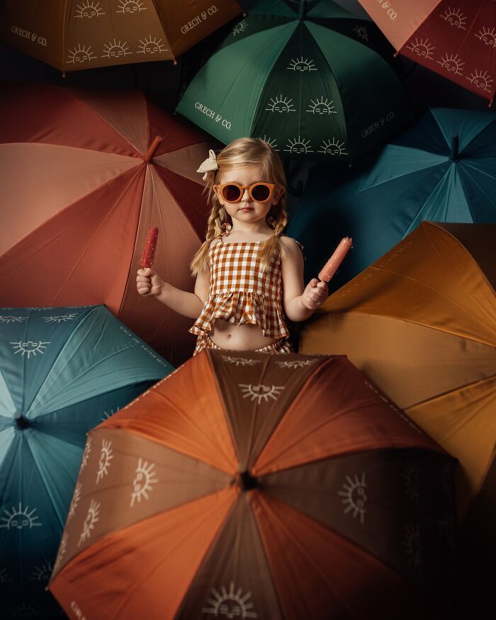 Child with popsicles and sunglasses, surrounded by colorful umbrellas, capturing the magic of childhood through photography.