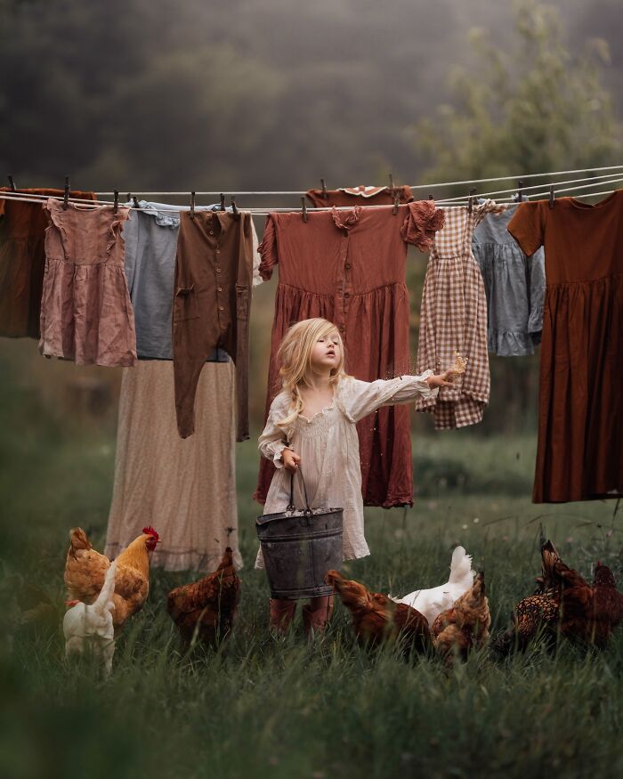 Childhood magic captured as a young girl, holding a bucket, stands among chickens under a clothesline in a rustic setting.