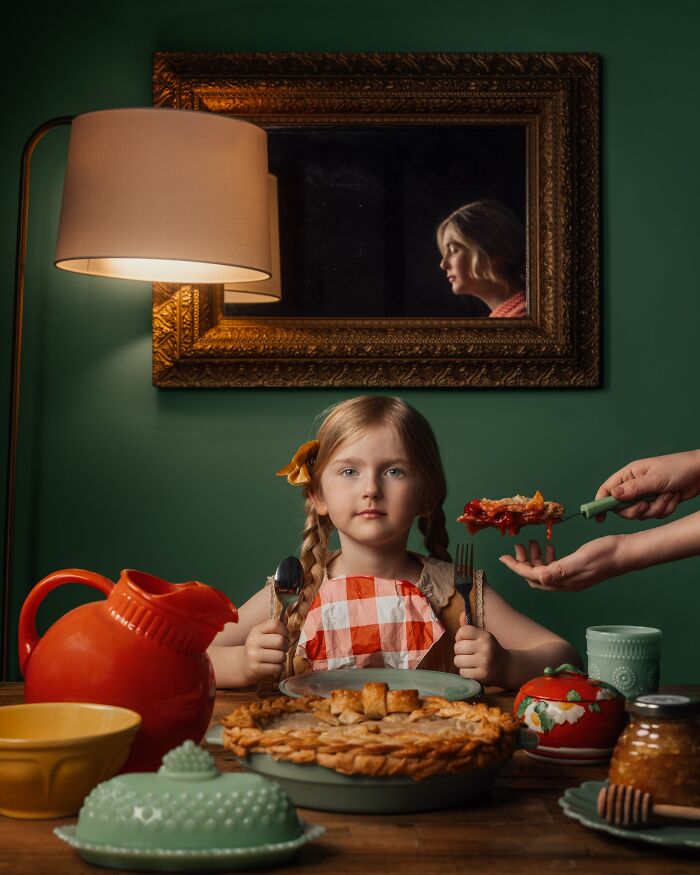 Child at a table with pie, surrounded by colorful dishes, showcasing childhood magic. A reflection of a woman in the mirror.