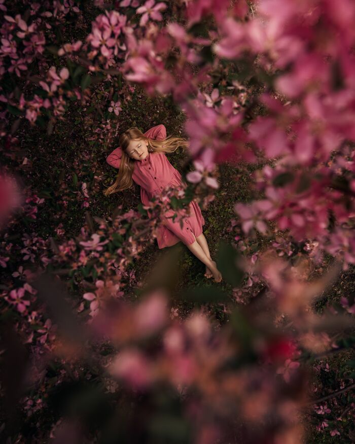 Child laying on grass surrounded by pink flowers, capturing childhood magic through a mother’s lens.