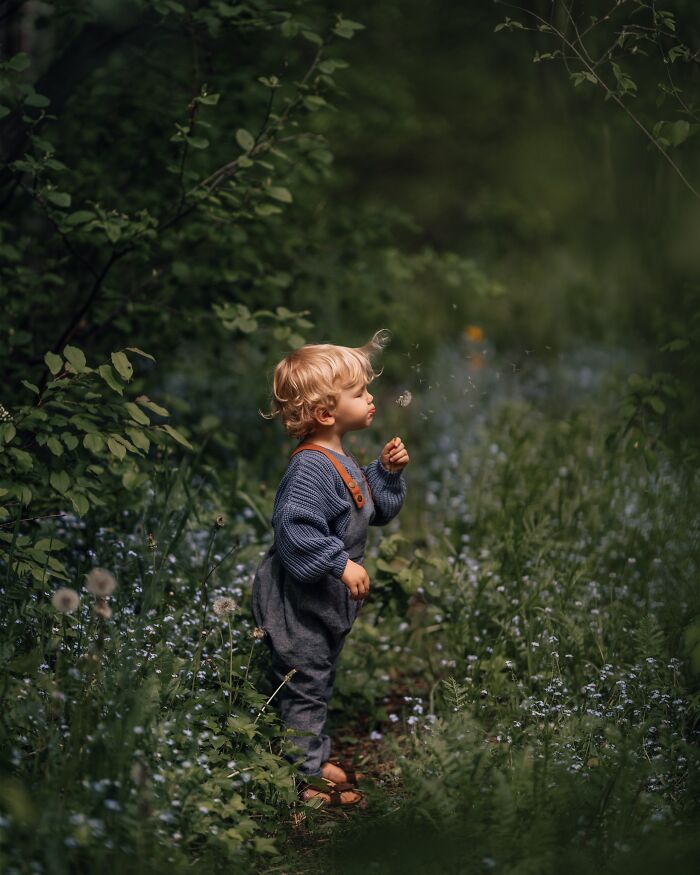 Child in a forest blowing on a dandelion, captured with the magic of childhood in a mother's lens.