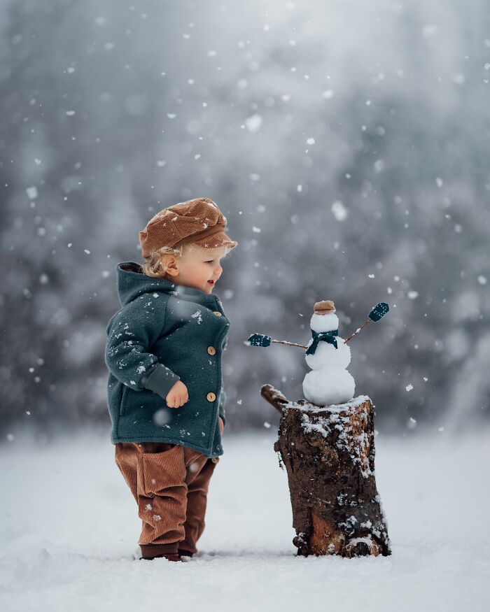 A child in a warm coat and cap admires a tiny snowman on a tree stump, capturing the magic of childhood in winter.