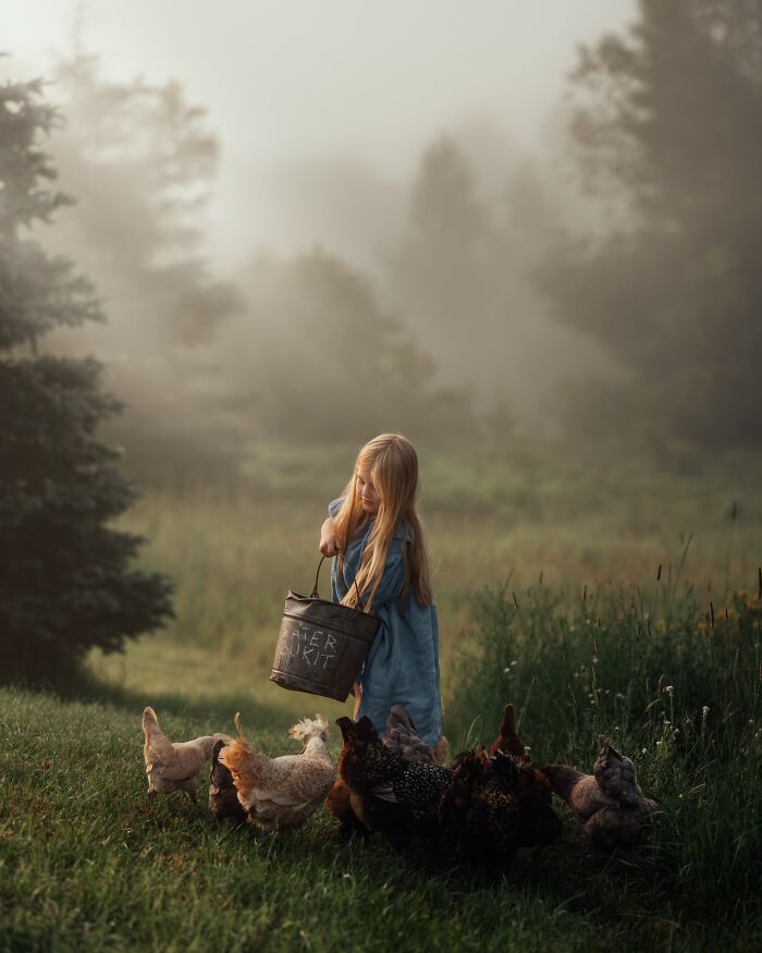 A child feeds chickens in a misty field, capturing the magic of childhood.