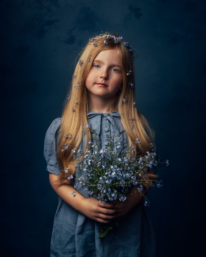 Child with long hair and a blue dress, holding flowers. Capturing the magic of childhood through a mother's lens.