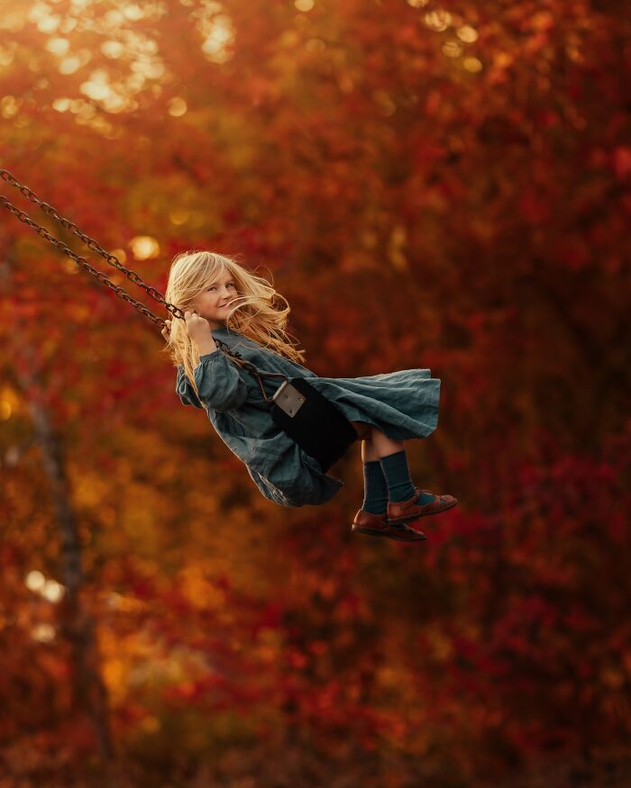 Child swinging joyfully in autumn forest, captured through a mother’s lens.