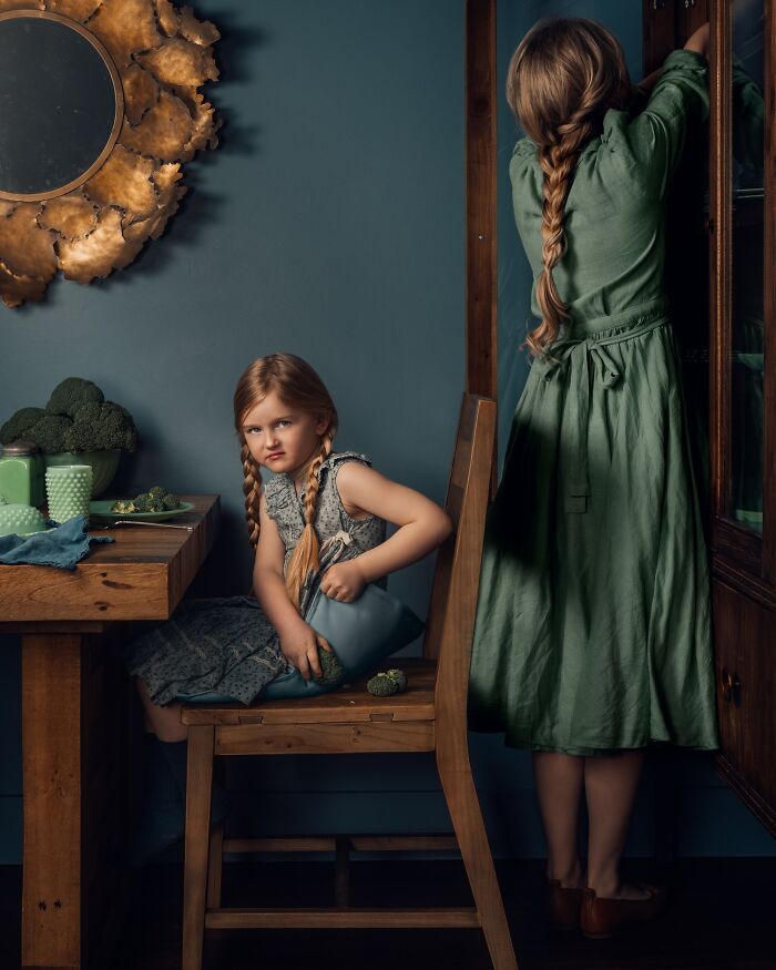 A mother captures the magic of childhood as her daughter sits with braided hair and vintage dress in a rustic kitchen setting.