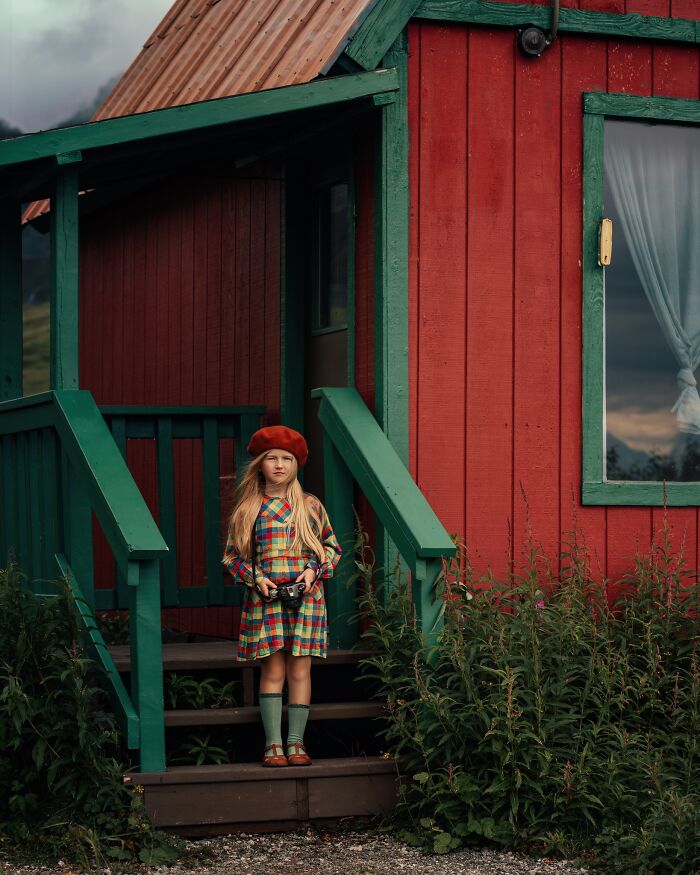 Child in vibrant outfit holding a camera, capturing the magic of childhood in front of a red house with green accents.