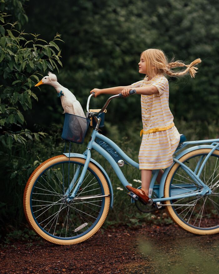 Child on a blue bicycle with a duck in the basket, capturing the magic of childhood in nature.