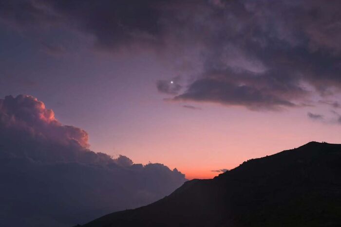 Night sky over mountains, showcasing astrophotography with a colorful sunset and emerging stars.