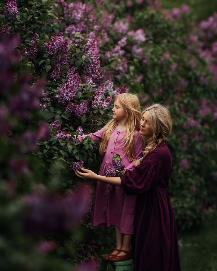A mother and child in purple dresses admire lilacs, capturing the magic of childhood in a garden setting.