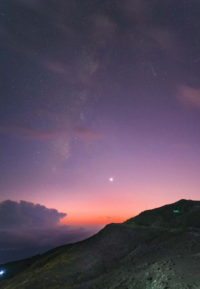 Astrophotography of a vibrant twilight sky with distant stars over a mountain silhouette.