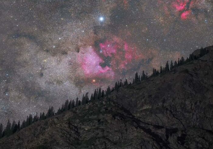 Night sky with a vibrant nebula over a silhouetted mountain ridge, showcasing astrophotography.