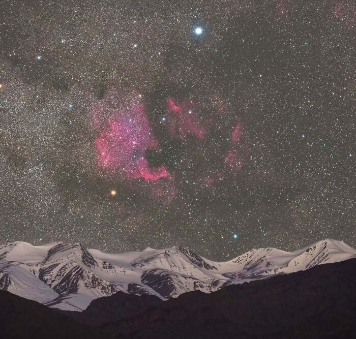 Starry night sky over snow-capped mountains in a stunning astrophotography scene.