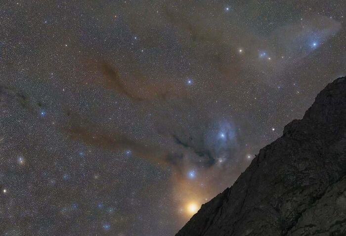 Night sky filled with stars and clouds over a rocky silhouette, capturing stunning astrophotography.