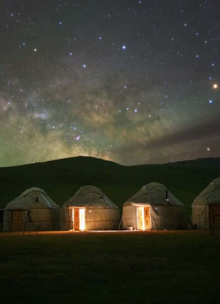 Astrophotography capture of glowing yurts under a starry night sky.