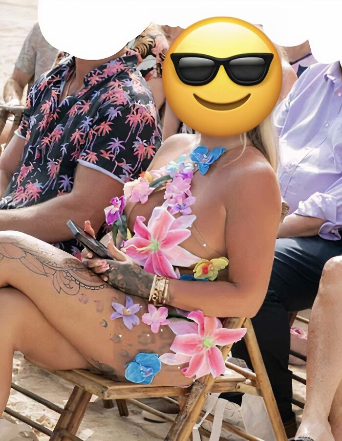 Guest at a wedding wearing a bold, floral outfit with a tattoo visible, sitting in a row of chairs outdoors.