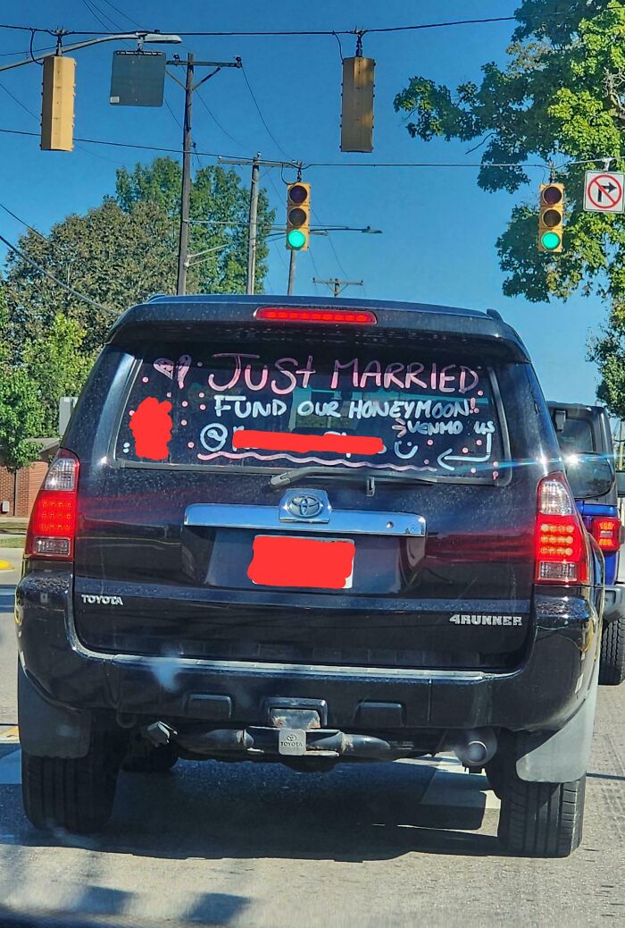 "Car with 'Just Married' sign and honeymoon donation request, highlighting a unique wedding moment."