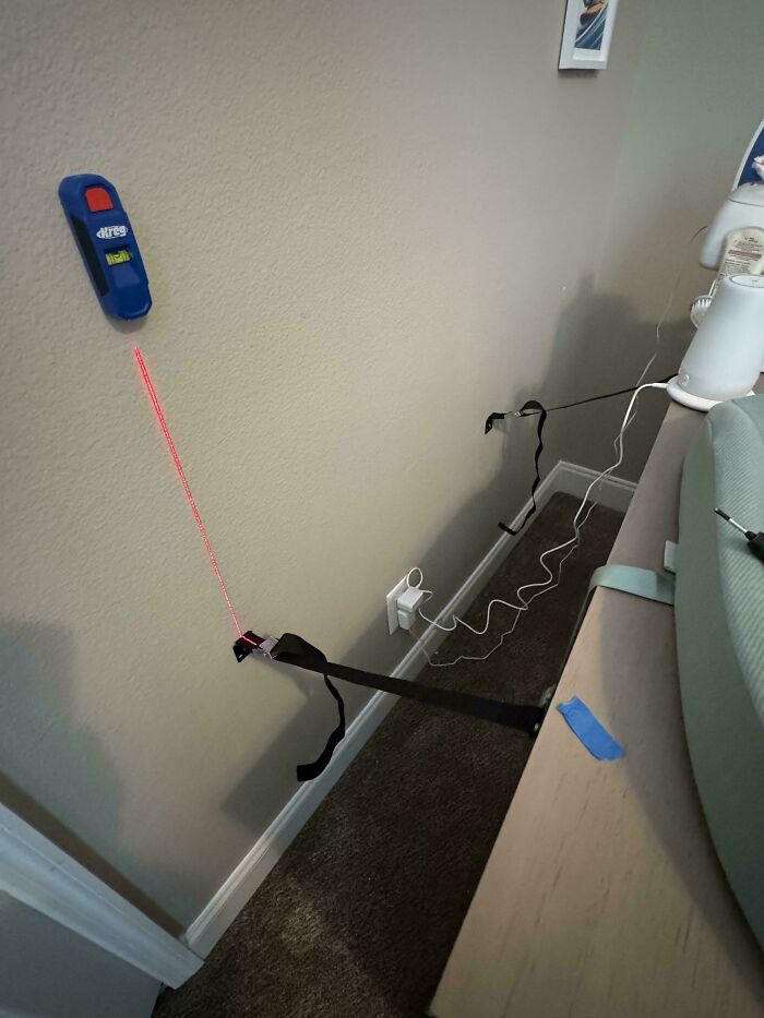 Laser level attached to wall with strap keeping furniture secure in a creative dads parenting moment.