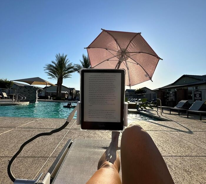 Reclining by a pool, person reads on a tablet under a small pink umbrella, one of those random Amazon finds.